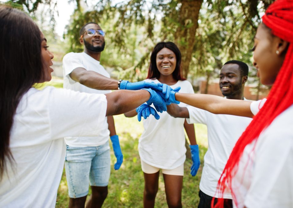 Group of happy african volunteers put hands in hands in park. Africa volunteering, charity, people and ecology concept.